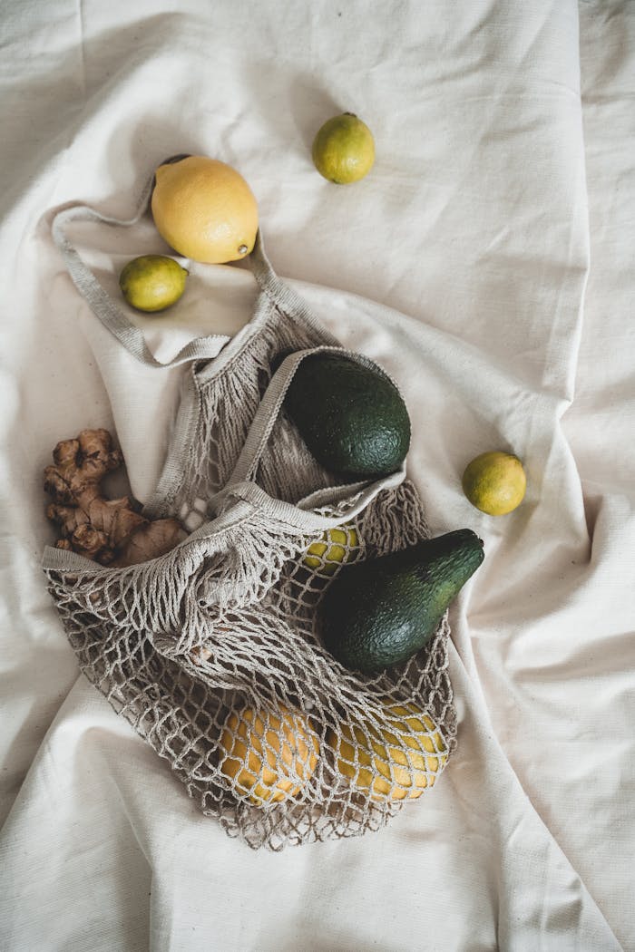 Net bag filled with avocados, lemons, ginger on a cloth, promoting zero waste shopping.